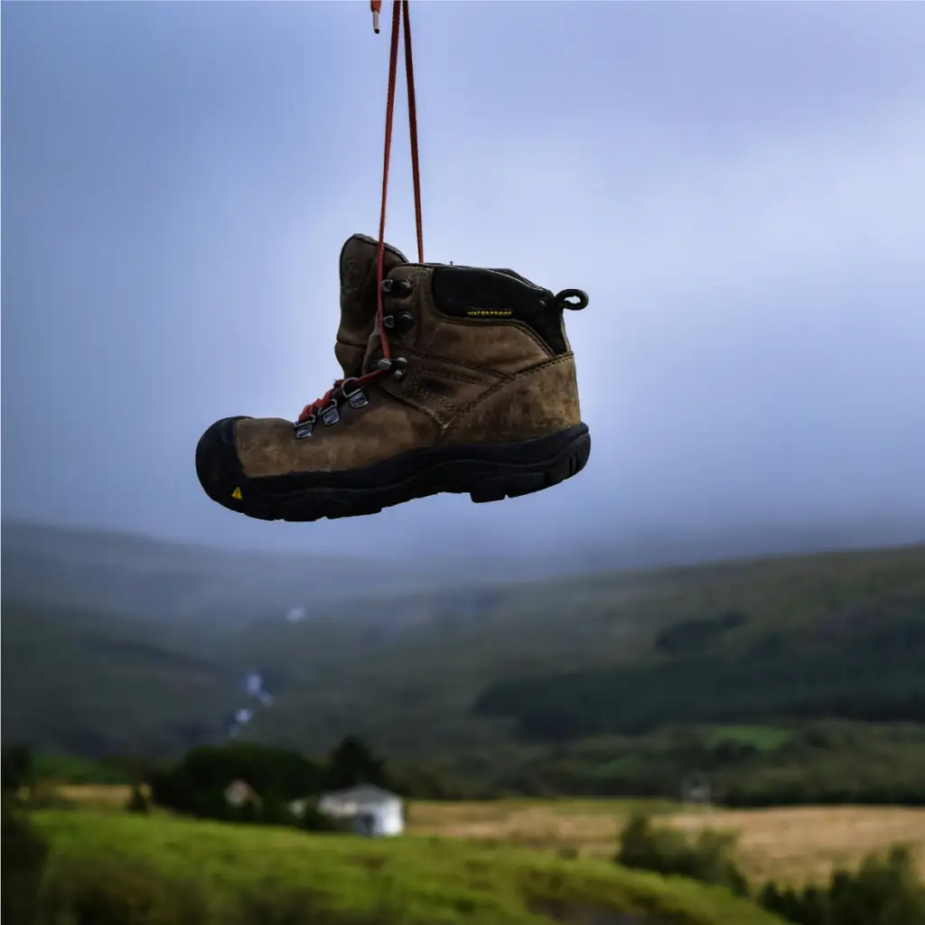 Une meilleure chaussure de randonnée suspendue par des lacets contre un paysage montagneux brumeux.