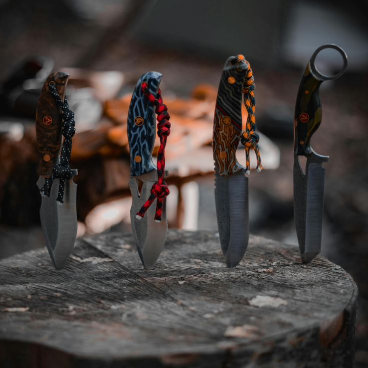 Four unique knives with differently designed handles, standing upright on a tree stump, against a blurred natural background.