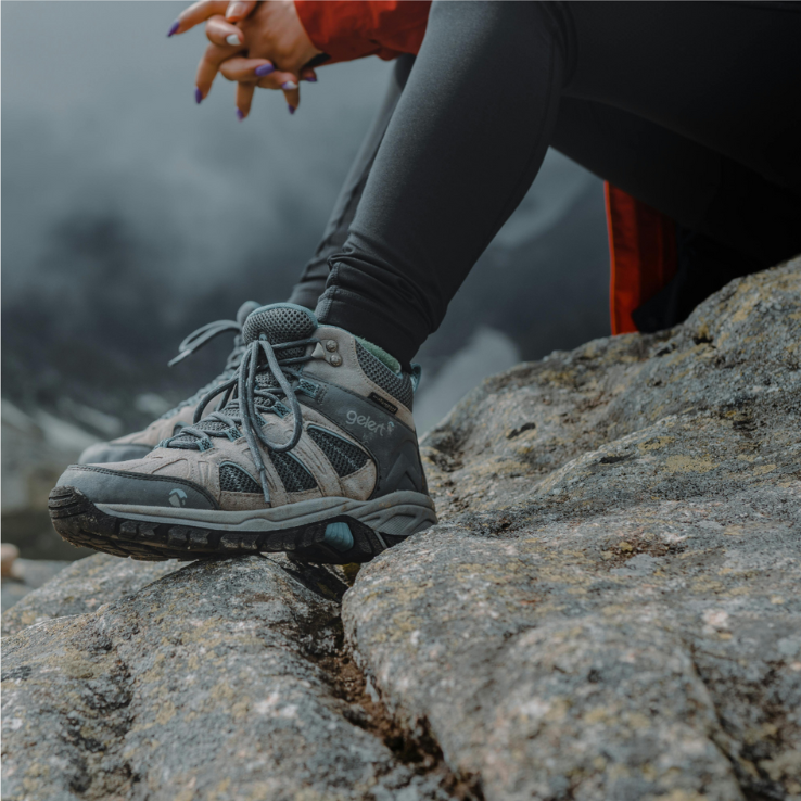 Close-up of a person's hiking boots on a rocky surface, with a misty mountain in the background, highlighting details such as laces and the sturdy sole.